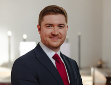 A headshot of Michael Graham in front of the sunlit altar of the Mary Harris Chapel. He wears a red tie, white shirt and a dark blue suit, and is smiling at the camera.